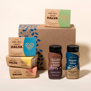 Assorted Seed + Mill products including Packages of Seed + Mill havla and tahini squeeze bottles on a beige background