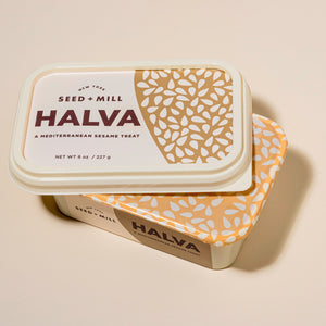 Container of opened Seed + Mill Halva on a beige background