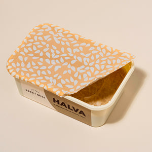 Container of opened halva with a patterned seal on a beige background