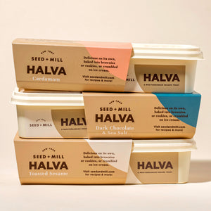 Stack of Seed + Mill Halva containers on a beige background