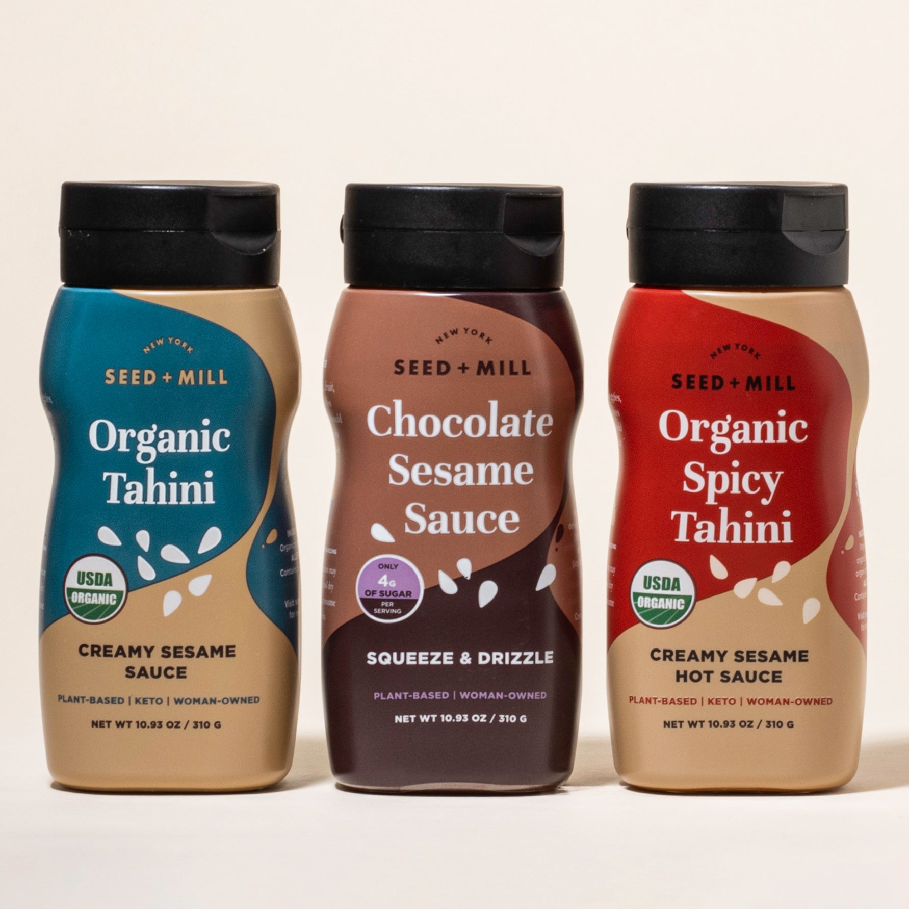 Three bottles of Seed + Mill Tahini, Organic Spocy Tahini, Chocolate Sesame Sauce, and Organic Tahini, on a beige background