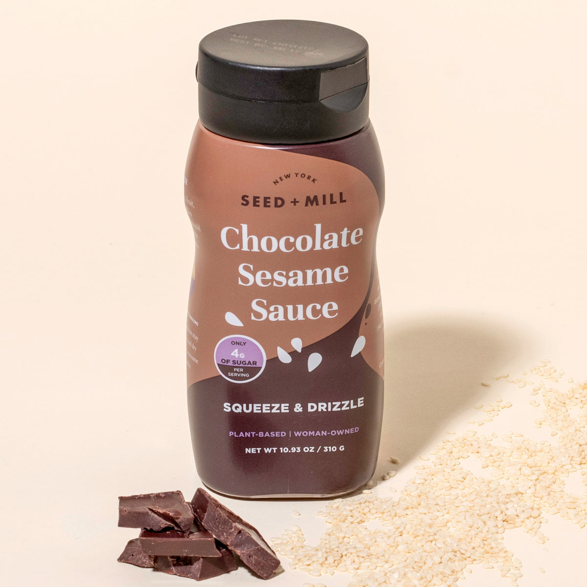Bottle of Seed + Mill Chocolate Sesame Sauce with ingredients on a beige background