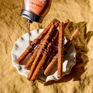A plate of pretzel sticks with chocolate sesame sauce being squeezed on top
