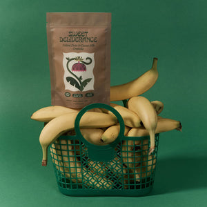 Sweet Deliverance Tahini Date & Cacao Nib granola package on top of a basket of bananas with a green background